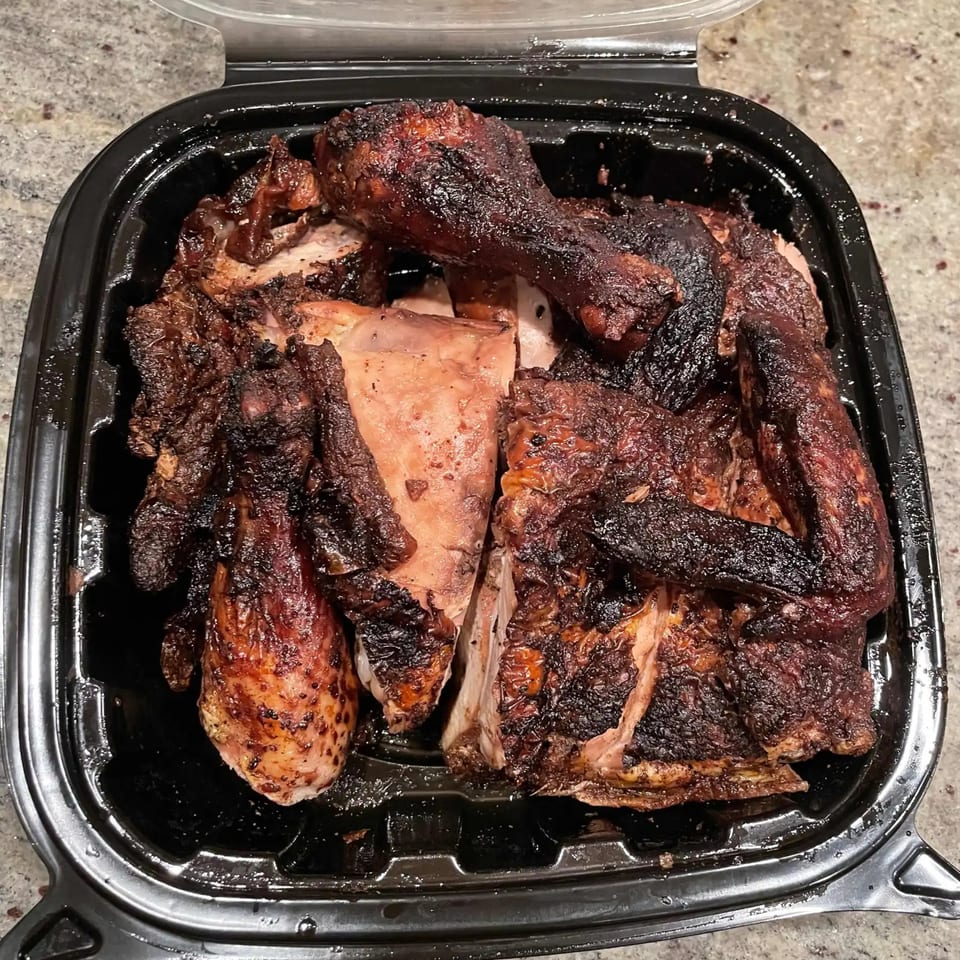 Jerk Villa Bar & Grill's Jamaican jerk chicken, dark and smoky, served in a black takeout container.