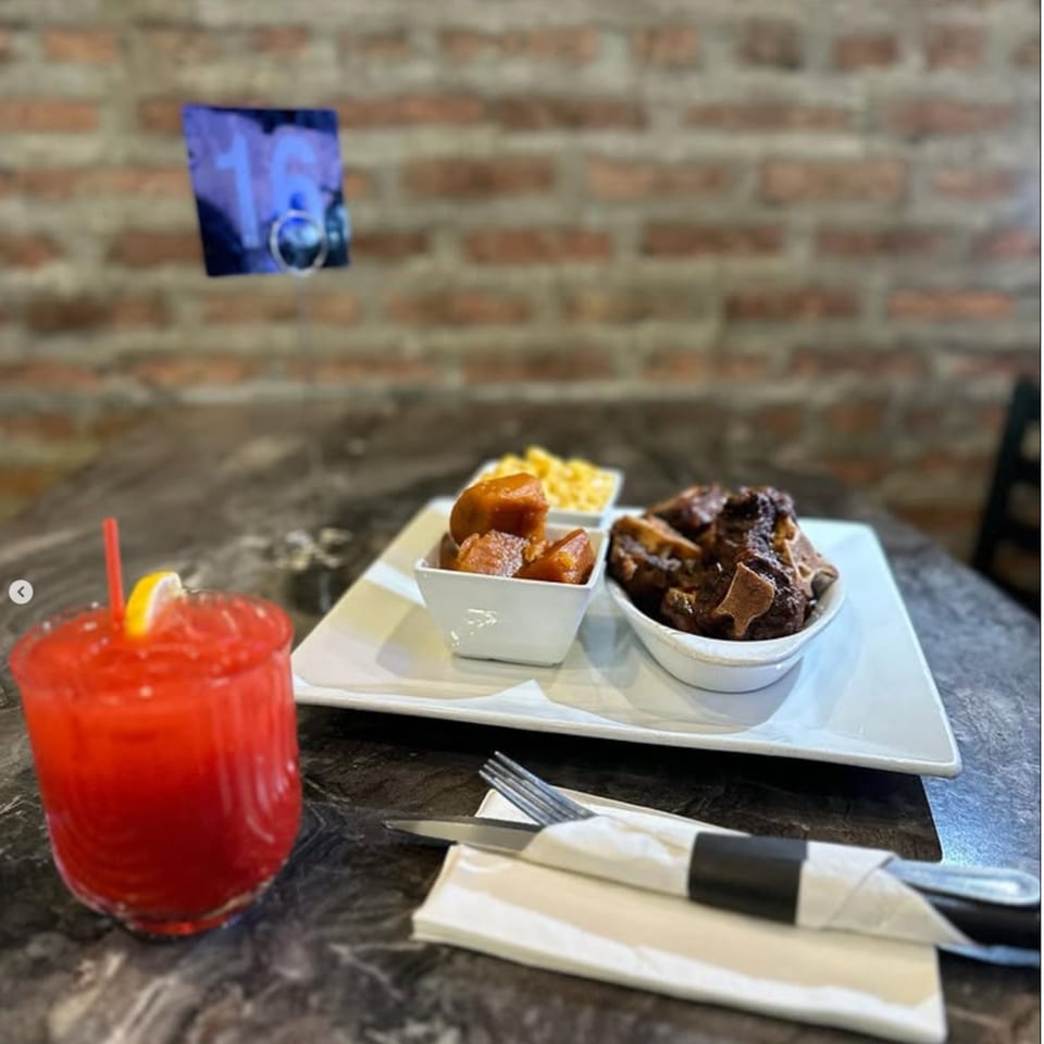 Jerk Villa Bar & Grill oxtail, candied yams, mac and cheese, and a red drink on a table.