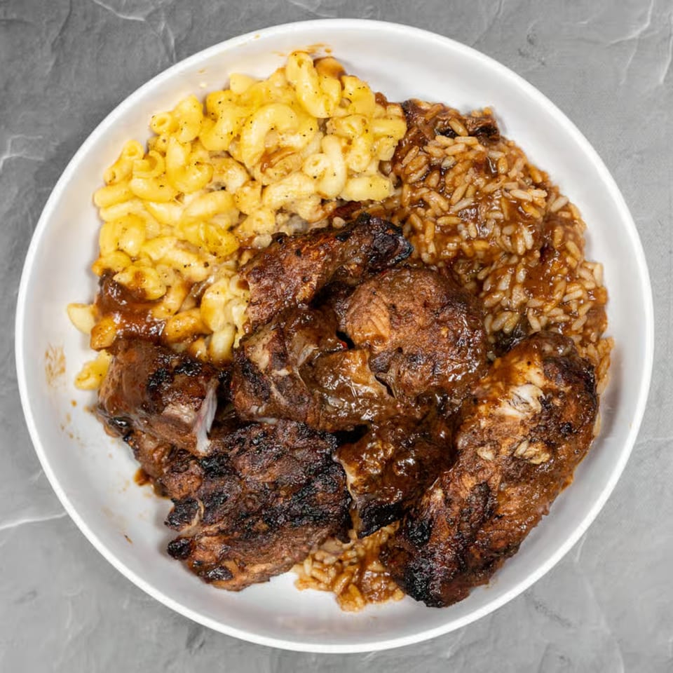 Jerk chicken with rice and peas, and macaroni and cheese in a white bowl.