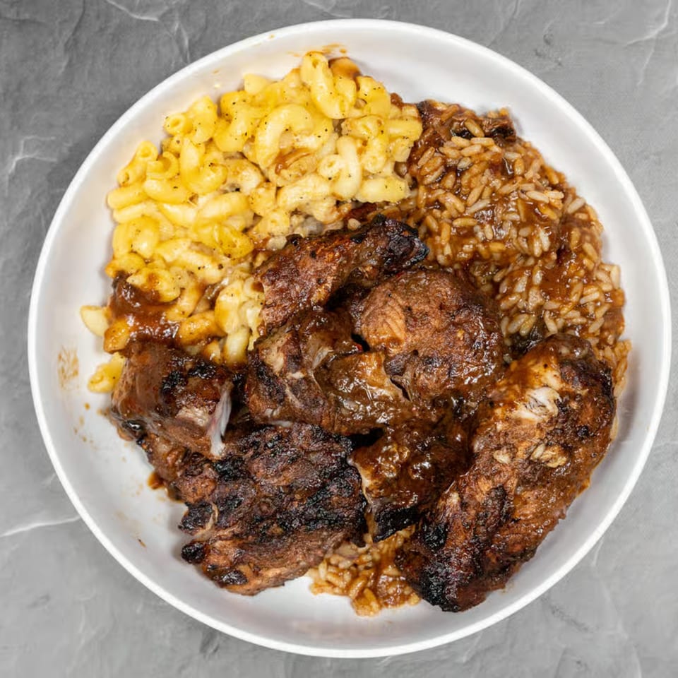 Jerk chicken with rice and peas, and macaroni and cheese in a white bowl.